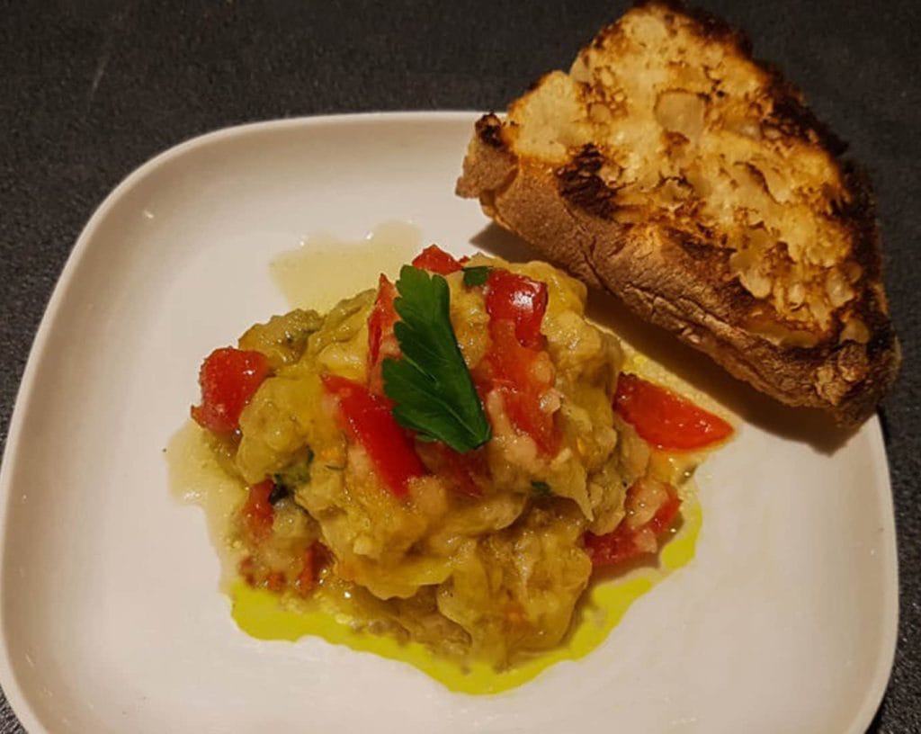 Domatesli, soğanlı, maydanozlu patlıcan salatası ızgara edilmiş bir ekmek dilimi ile servis ediliyor