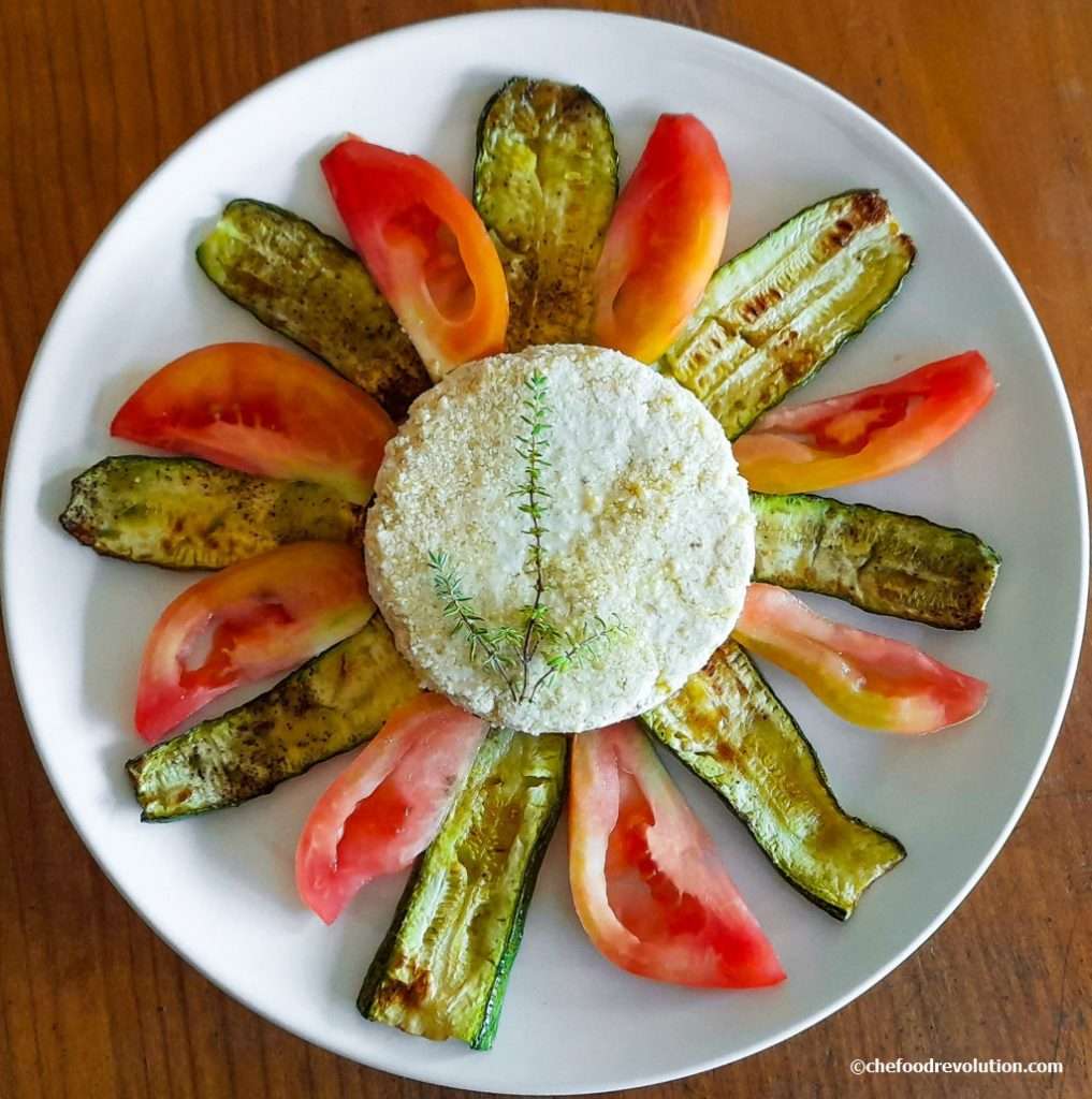 Beautiful dish with a homemade round tofu block in the middle of a plate of tomatoes and courgettes, forming a sun and its rays