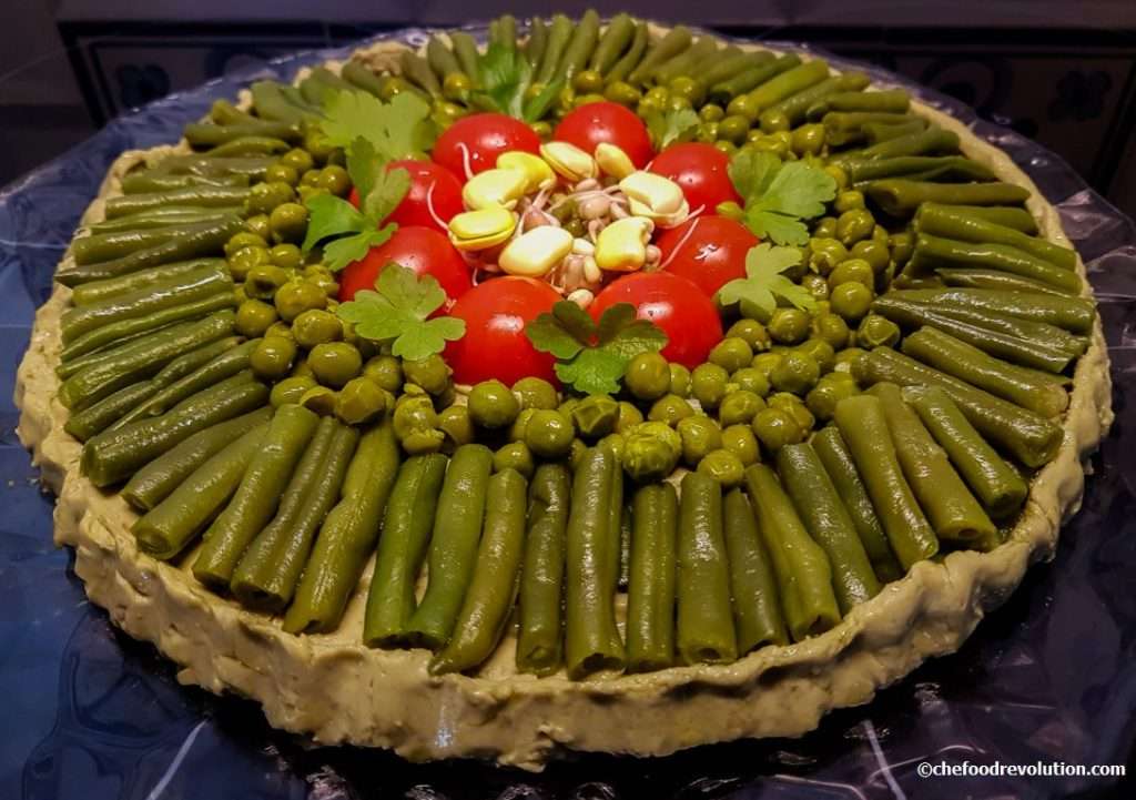 Favalı meze domates, börülce, bezelyeö acı bakla, maş fasulyesi filizi gibi malzemelerle bir pasta gibi özenle süslenerek servis ediliyor
