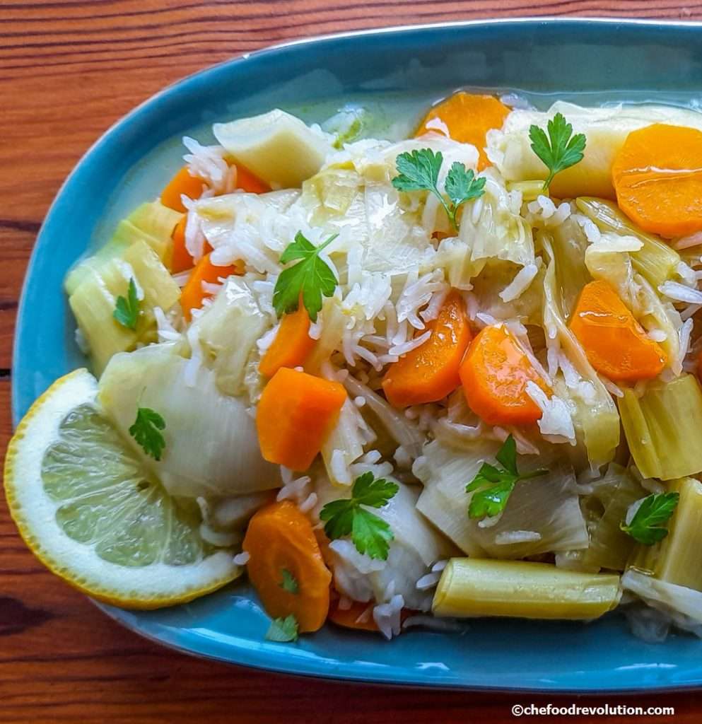 on a plate braised leeks and carrots and rice served with citrus sauce, a lemon wedge and parsley leaves