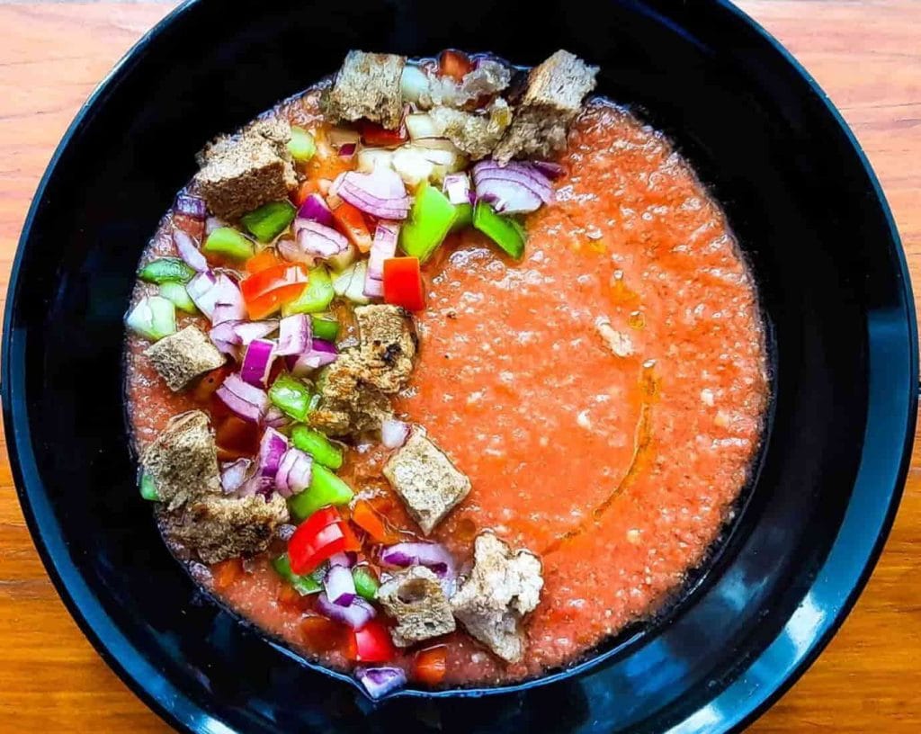 zuppa di gazpacho con cubetti di pane e verdure in un piatto nero