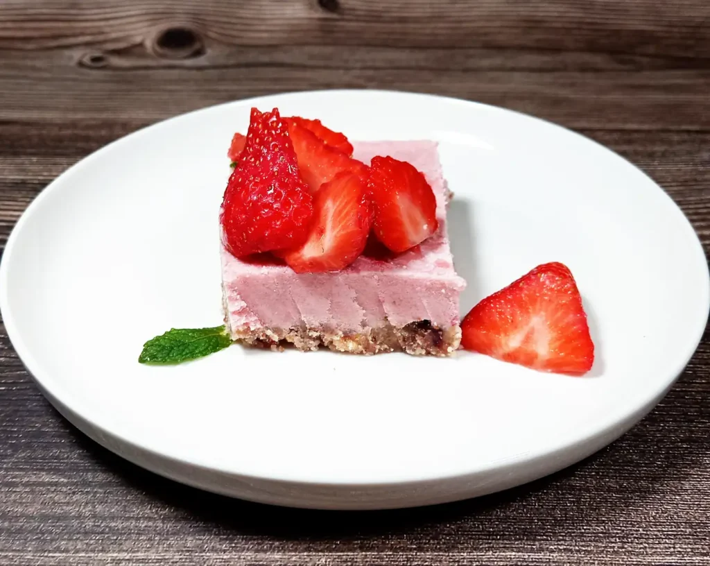 Enfes bir vegan çilekli cheesecake dilimi çilekler ve fesleğen yaprağı ile servis edilmekte