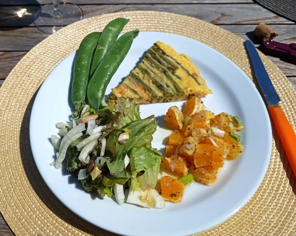 What to eat in May is shown in a yummy plate of fresh peas, asparagus chickpea omelette, orange, spring onions, lettuce salad