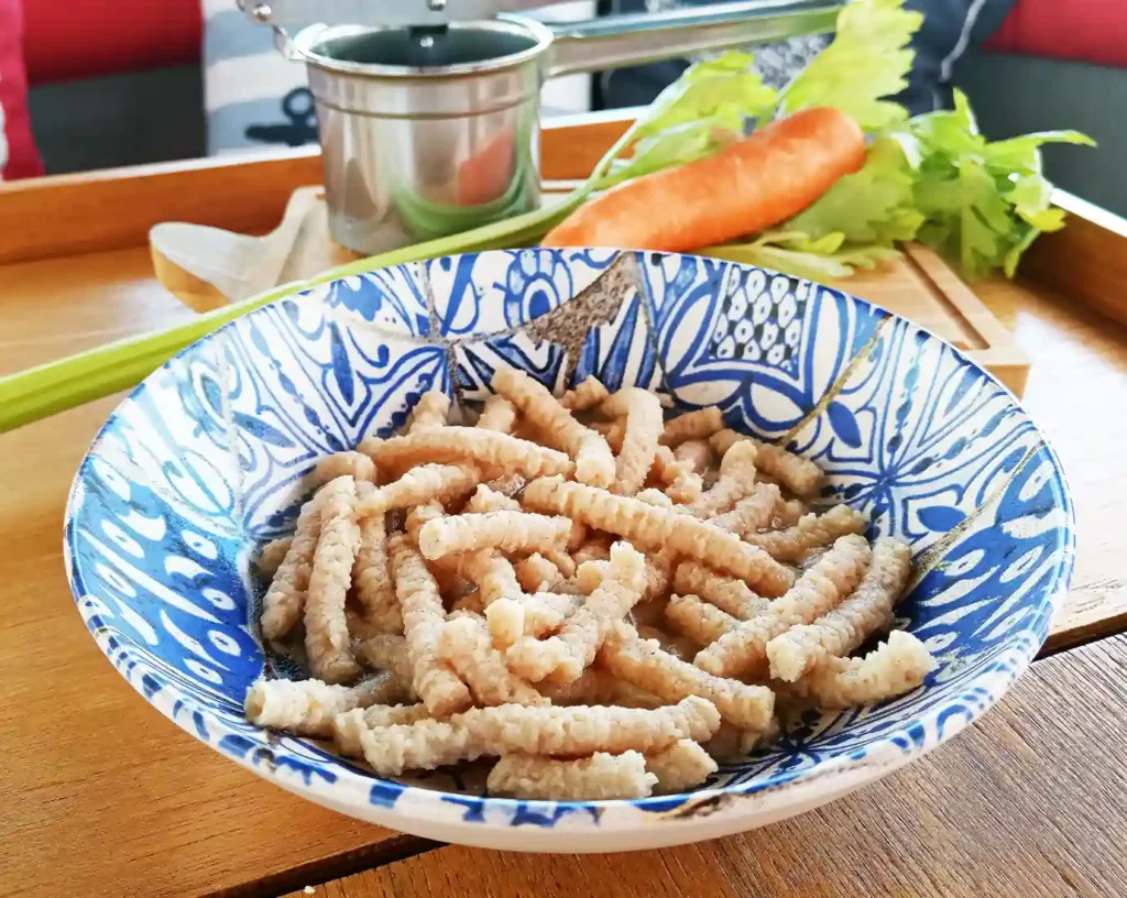 I passatelli facili sono serviti in un piatto, e allo sfondo si vedono le carote, sedano e utensile specifico per i passatelli